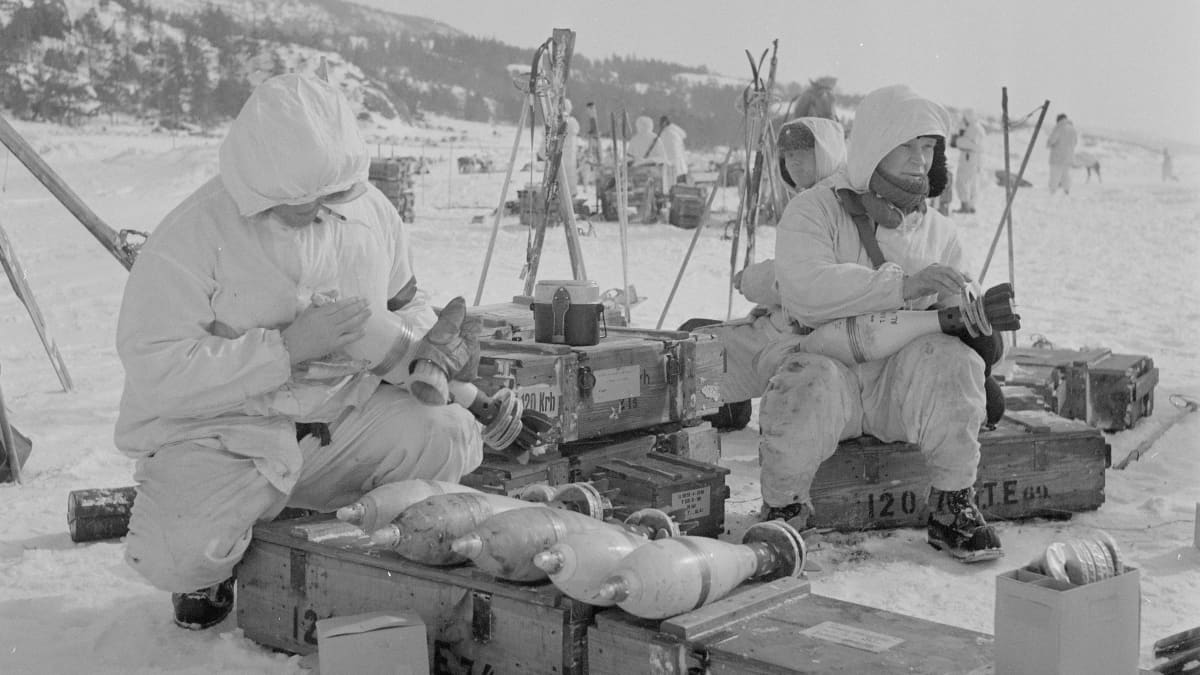 Suomalaisia sotilaita vuonna 1942 meren jäällä valkoisissa talvipuvuissaan. Istuvat laatikoiden päällä ja käsittelevät granaatteja..