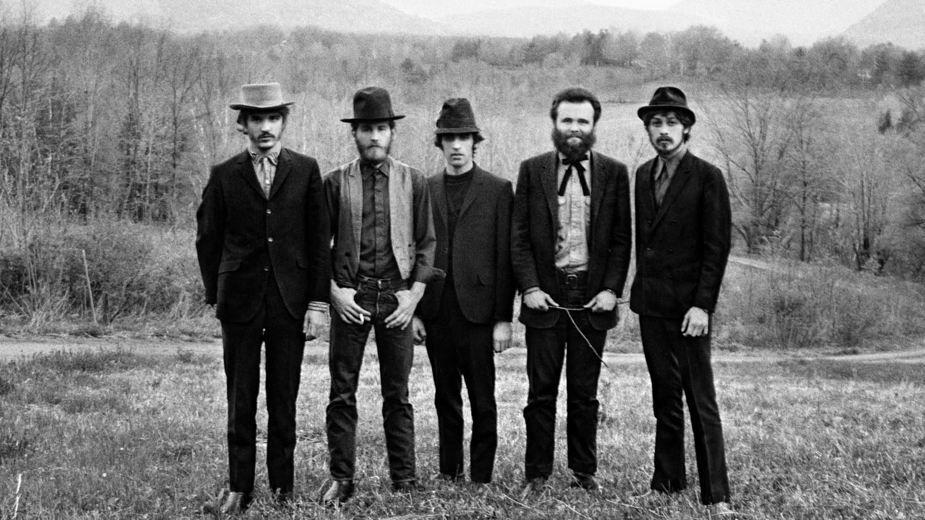 The Band-yhtyeen jäsenet eli viisi miestä seisoo rinnakkain mustavalkoisessa kuvassa, joka on otettu maalaismasemassa. 