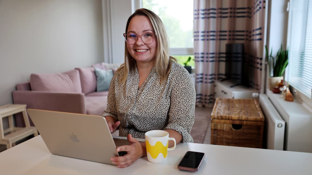 Digimarkkinointia työkseen tekevä Eevi Roivainen hymyilee kotonaan tietokoneensa ääressä.