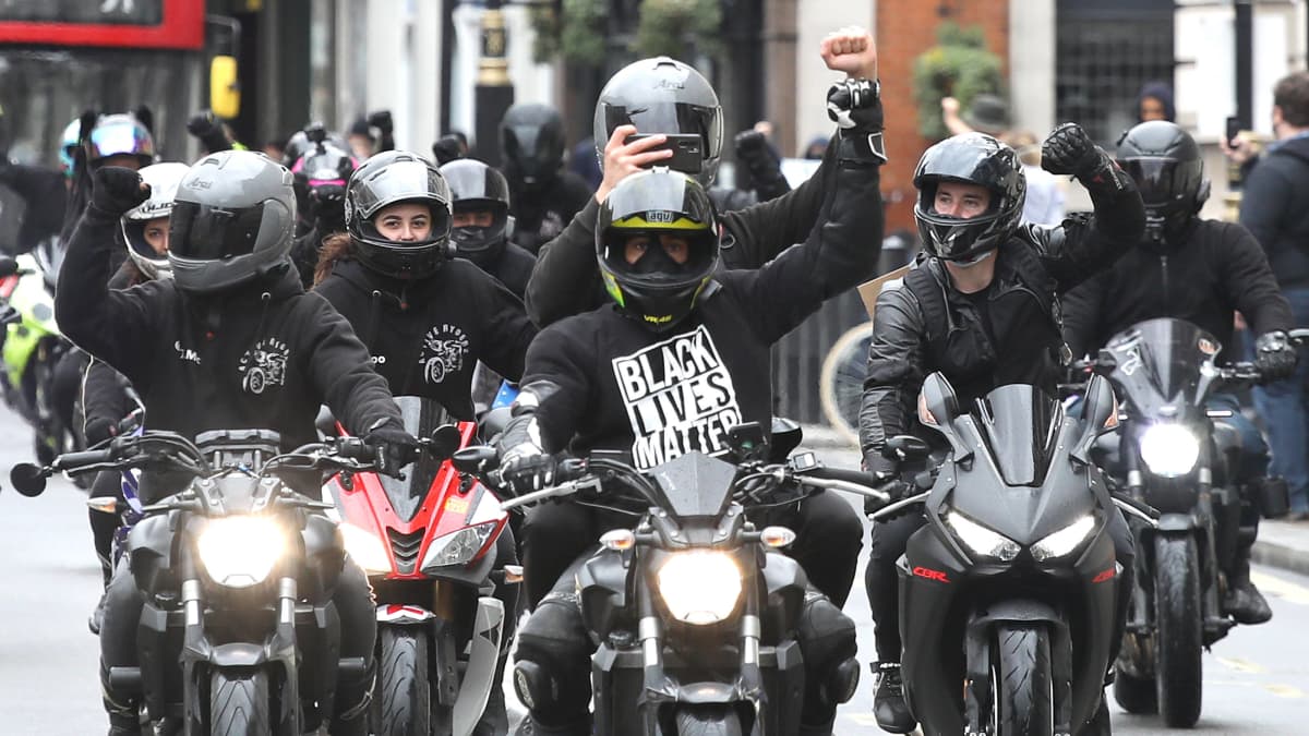 Joukko mustiin pukeutuneita moottoripyöräilijöitä nyrkkiin puristetut kädet koholla.