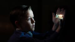 En liten pojke håller upp sina händer i mörkret och på handflatorna projiceras en film.
