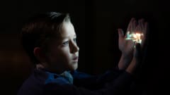 En liten pojke håller upp sina händer i mörkret och på handflatorna projiceras en film.