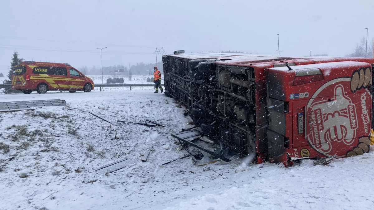 Kaatunut linja-auto lumisella tien pientareella, ambulanssi ja pelastusviranomainen.