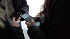 Tre unga tjejer med svarta jackor håller i mobiltelefoner.