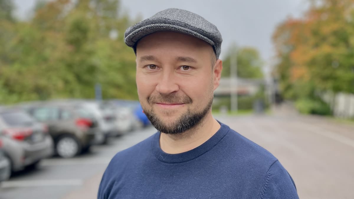 Siniseen neuleeseen ja harmaaseen lakkiin sonnustautunut ylöjärveläinen Tommi Tapio katsoo kameraan. Taustalla näkyy parkkipaikka.