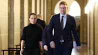 A woman in black and a taller man in a blue suit and glasses walking in a corridor at the Parliament building.