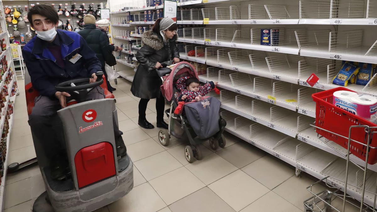 Siivooja puhdistaa lattioita ja asiakkaat kulkevat tyhjiin hamstrattujen hyllyjen ohi Auchan-ketjun marketissa keskiviikkona, Podolskissa, Moskovan ulkopuolella.