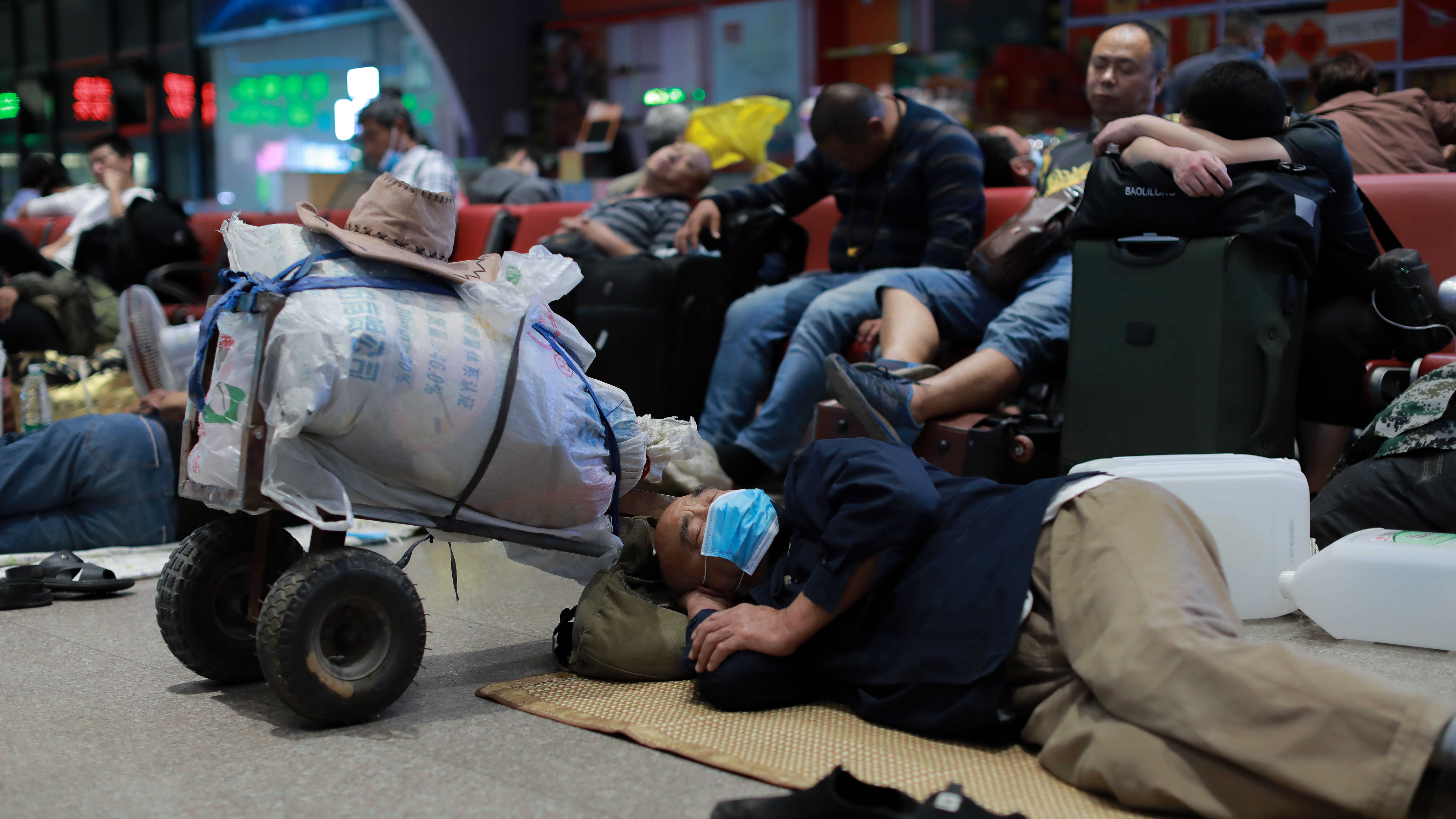 Mies nukkuu juna-aseman lattialla ohuen peiton päällä. Hänen vieressään on matkatavaroita pakattuna riisisäkkiin.