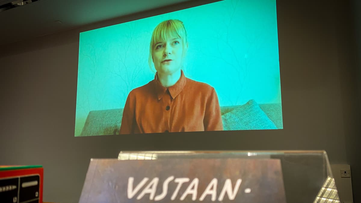 Sarjakuva-Finlandian voittaja Suvi Ermilä näkyy videoyhteyn välityksellä ruudulla. Alla Ermilän teos "Vastaanottokeskus"