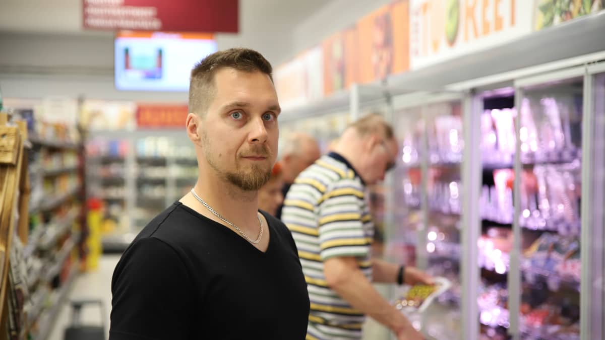 K-Market Sinetän kauppias Ville Mölläri kaupan käytävällä ja taustalla asiakkaita.
