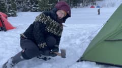 Reetta Muranen hakkaa teltan naruja piteleviä nauloja jäähän kirveen hamaralla.