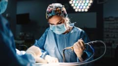 En kirurg håller i ett verktyg och tittar ner på en kropp.