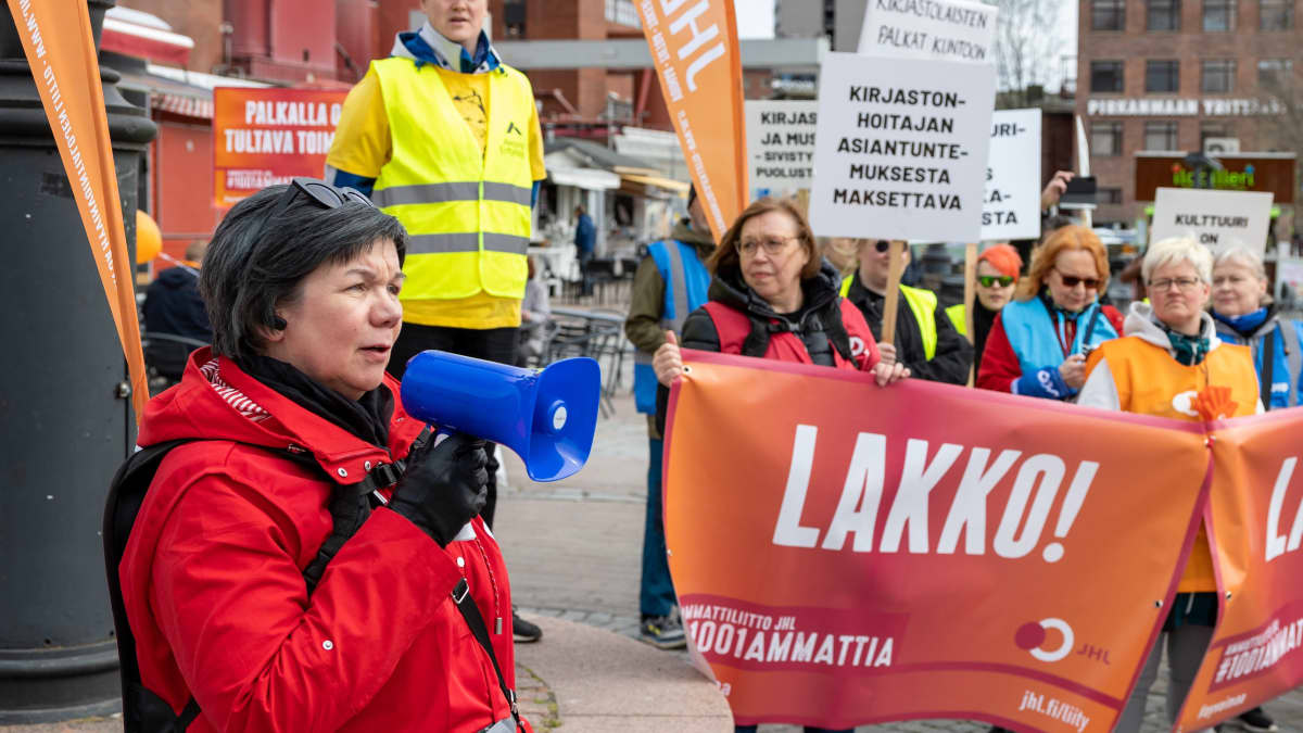 Ihmisiä kokoontuneena lakkomarssille Tampereella. Kylttejä, joissa lukee "Lakko". Nainen puhuu megafoniin. 