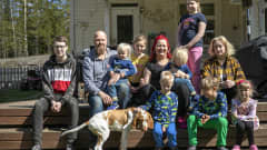 Sanna ja Juha Salin yhdeksän lapsensa kanssa yhteiskuvassa talonsa terassin rappusilla.