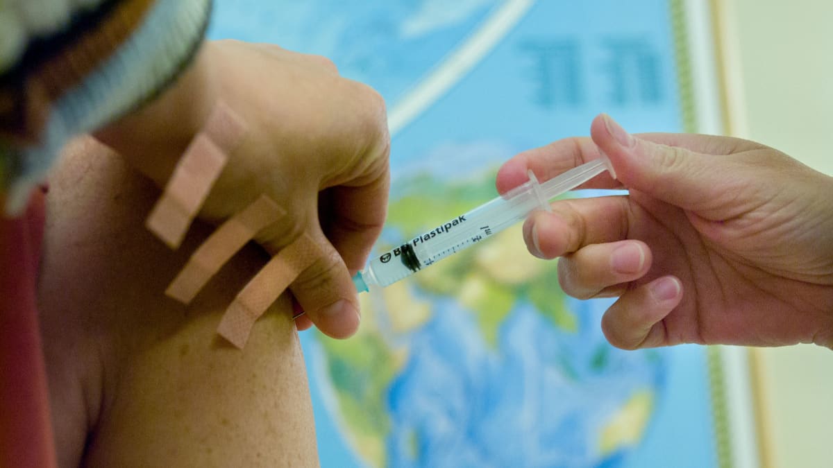 En läkare som sprutar in vaccin, genom en spruta, in i armen på en patient.