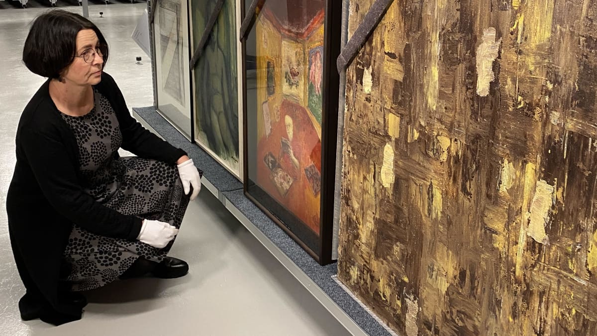 Kokoelmapäällikkö Sari Kainulainen katselee kokoelmaan kuuluvia maalauksia