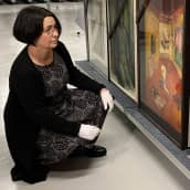 Kokoelmapäällikkö Sari Kainulainen katselee kokoelmaan kuuluvia maalauksia