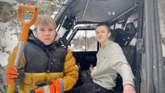 Leevi Heikkinen oranssi-mustassa talvitakissa koppimönkijän edessä lapio kädessä, taustalla Viljam Erkkilä koppimönkijän ratissa.