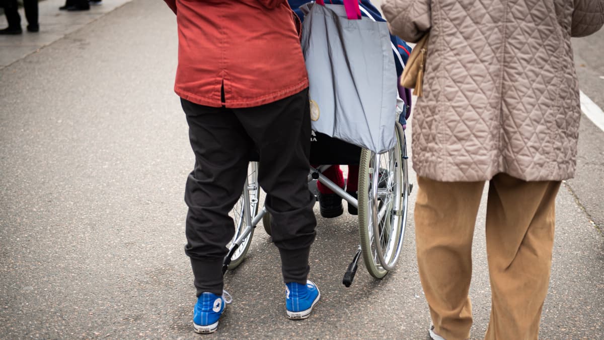 Nainen työntää vanhusta pyörätuolissa olevaa vanhusta.