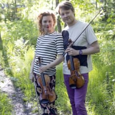 Kaksi ihmistä seisoo kesäisellä polulla viulut käsissään.