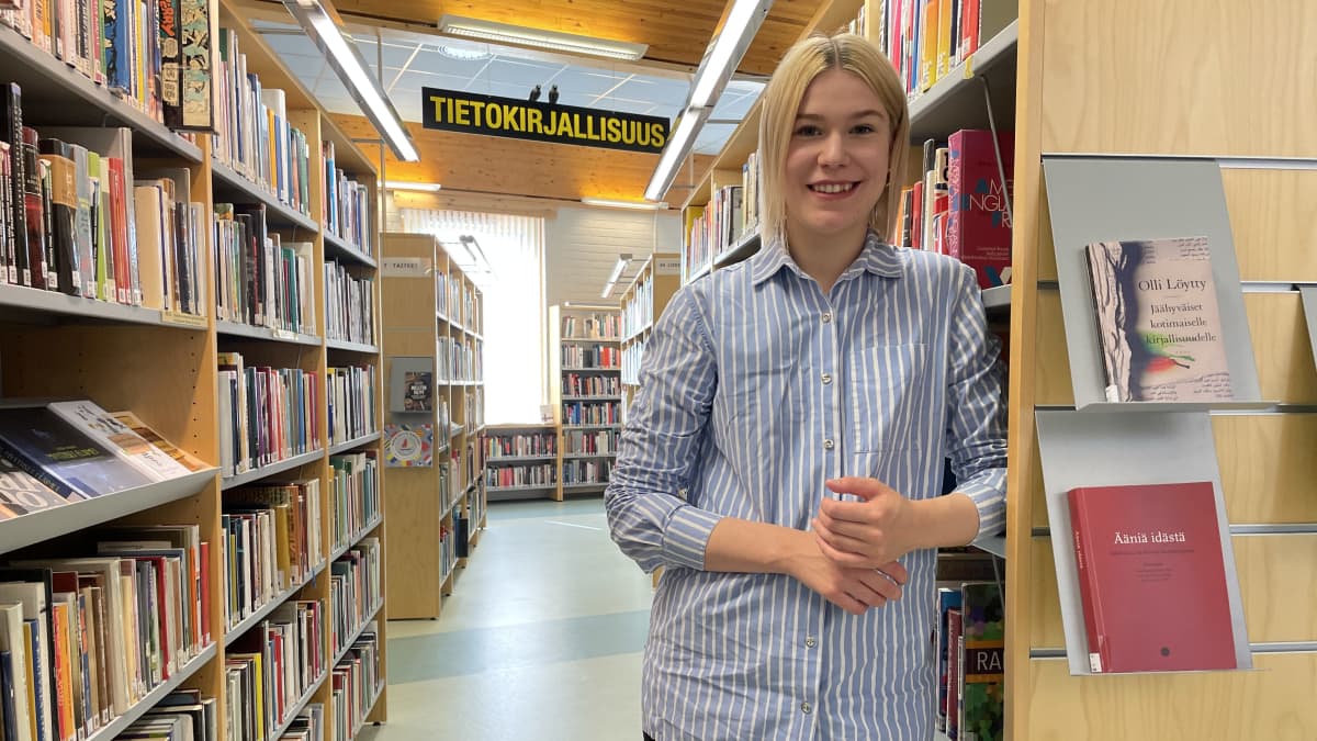 Suomussalmen uusi kunnanvaltuutettu Milla Veteläinen seisoo kirjaston hyllyjen välissä ja katsoo hymyillen suoraan kameraan.