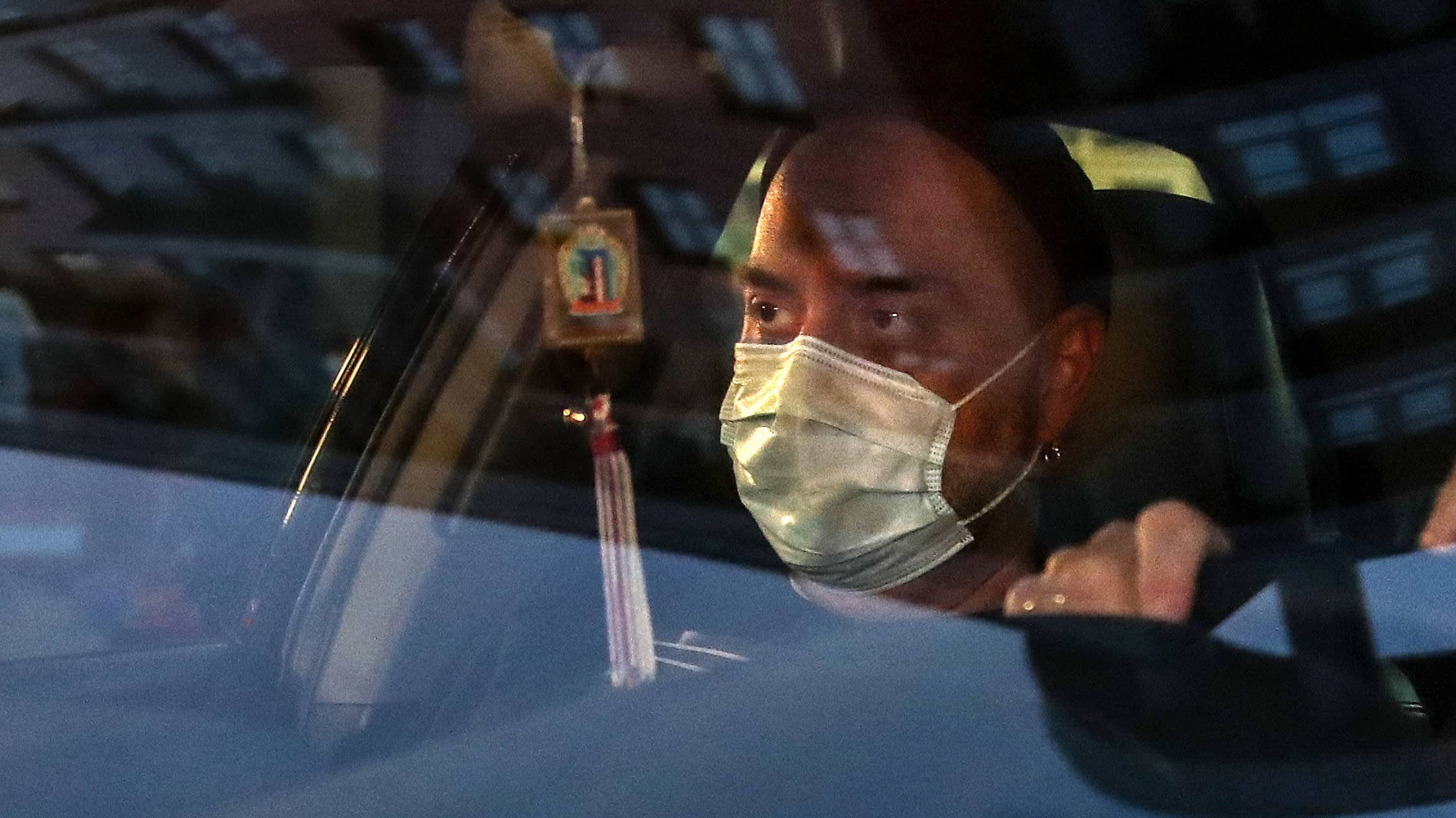 Mies istuu autossa maski kasvoillaan