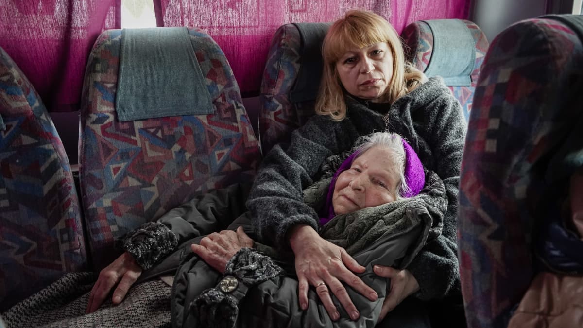 Vanha nainen lepää pää nuoremman naisen sylissä bussin takapenkillä.
