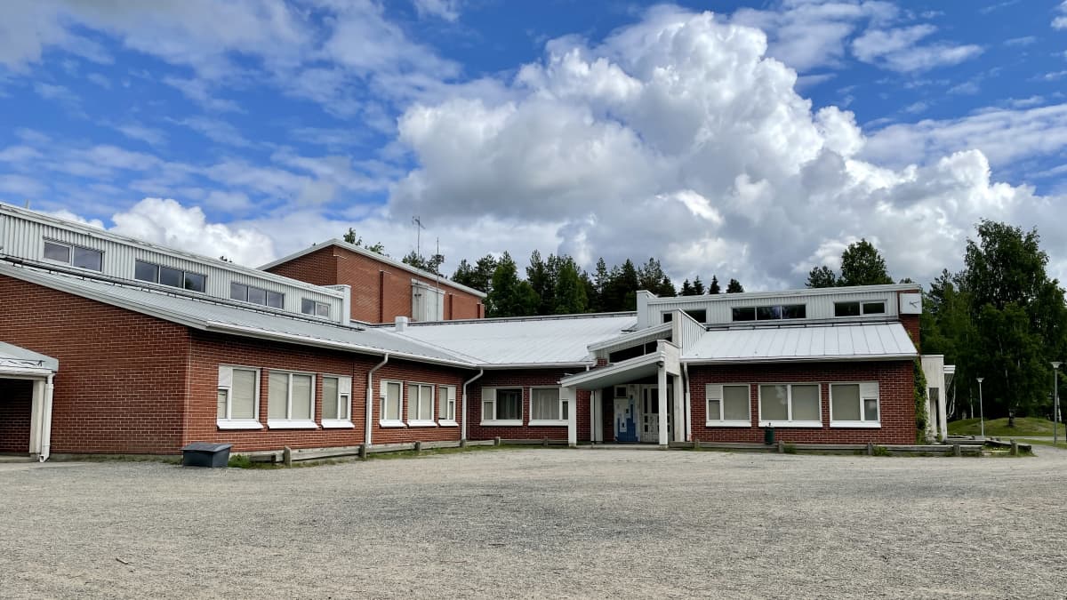 Punatiilinen koulurakennus kesällä, sinisella taivaalla iso valkoinen pilvi.