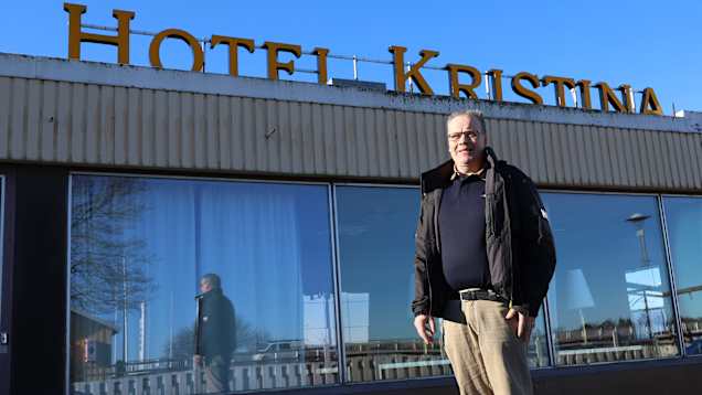 En man står utanför en byggnad. Ovanpå byggnaden står en skylt med texten hotell Kristina.