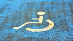 En vit rullstol målad på blått underlag på en parkeringsplats.