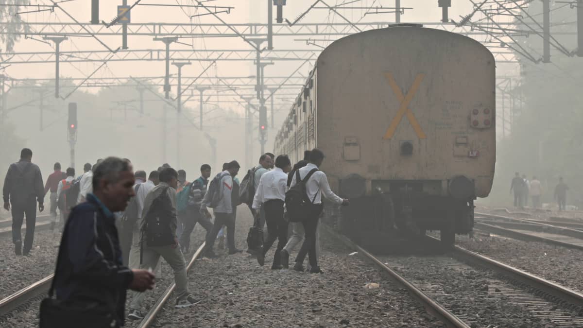 Työmatkalaiset kävelevät junaradalla lähellä rautatieasemaa paksun savukerroksen peittäessä kaupungin Intian New Delhissä 5. marraskuuta 2022.