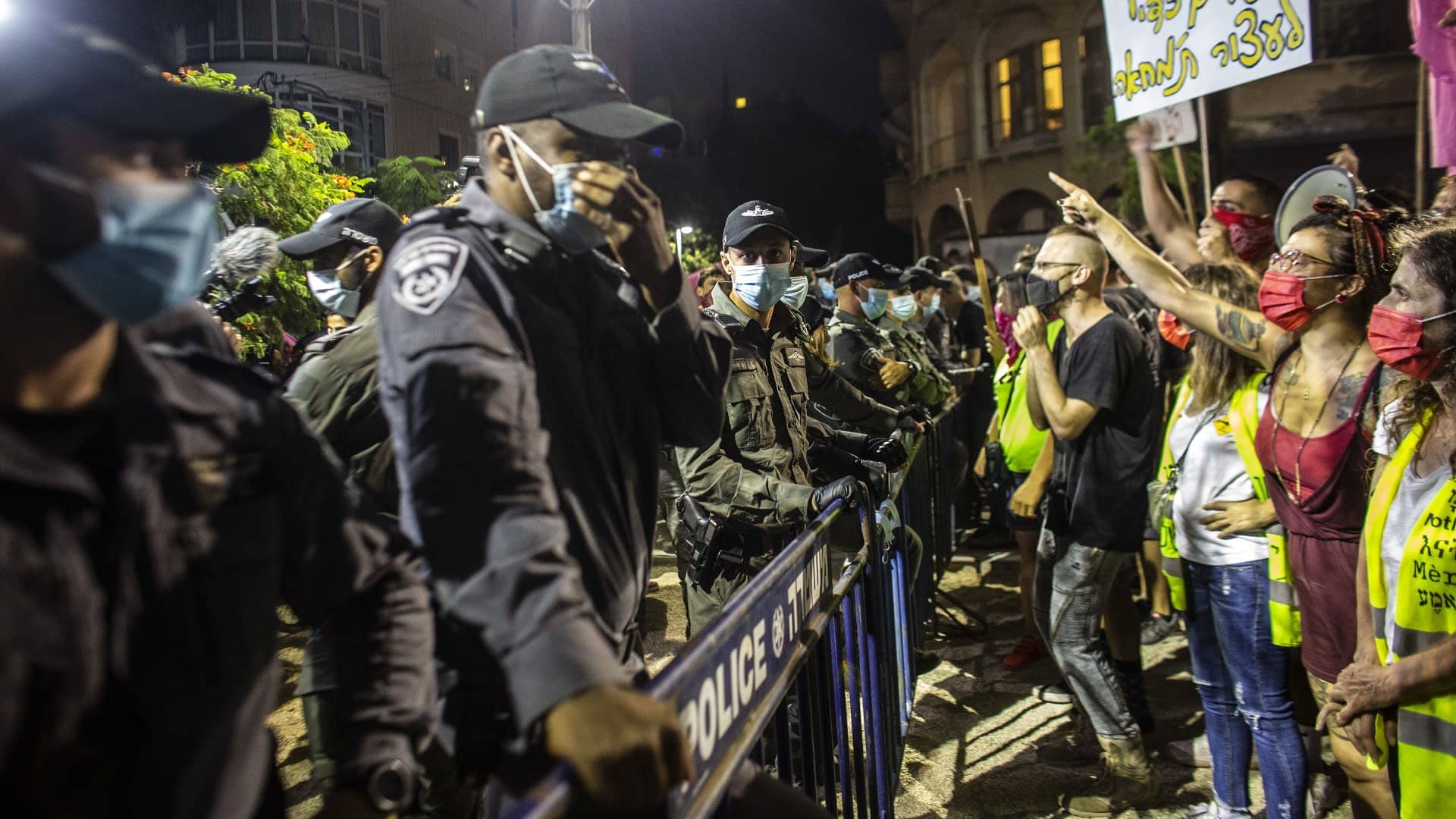 Mielenosoittajia aidan toisella puolen, toisella puolella on poliiseja.