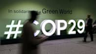Henkilöitä kävelemässä COP29-konferenssin kyltin edessä.
