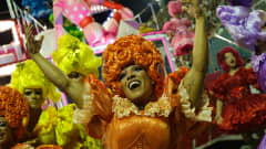 Rion karnevaalien esiintyjiä punaisessa, oransseissa ja keltaisissa röyhelöasuissa tanssivat.