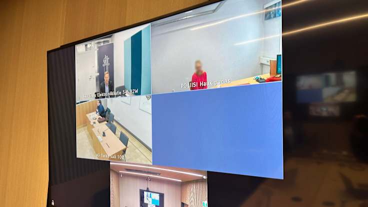 Photo of a television screen displaying four chat windows, each of which showing people sitting at desks during a court hearing.