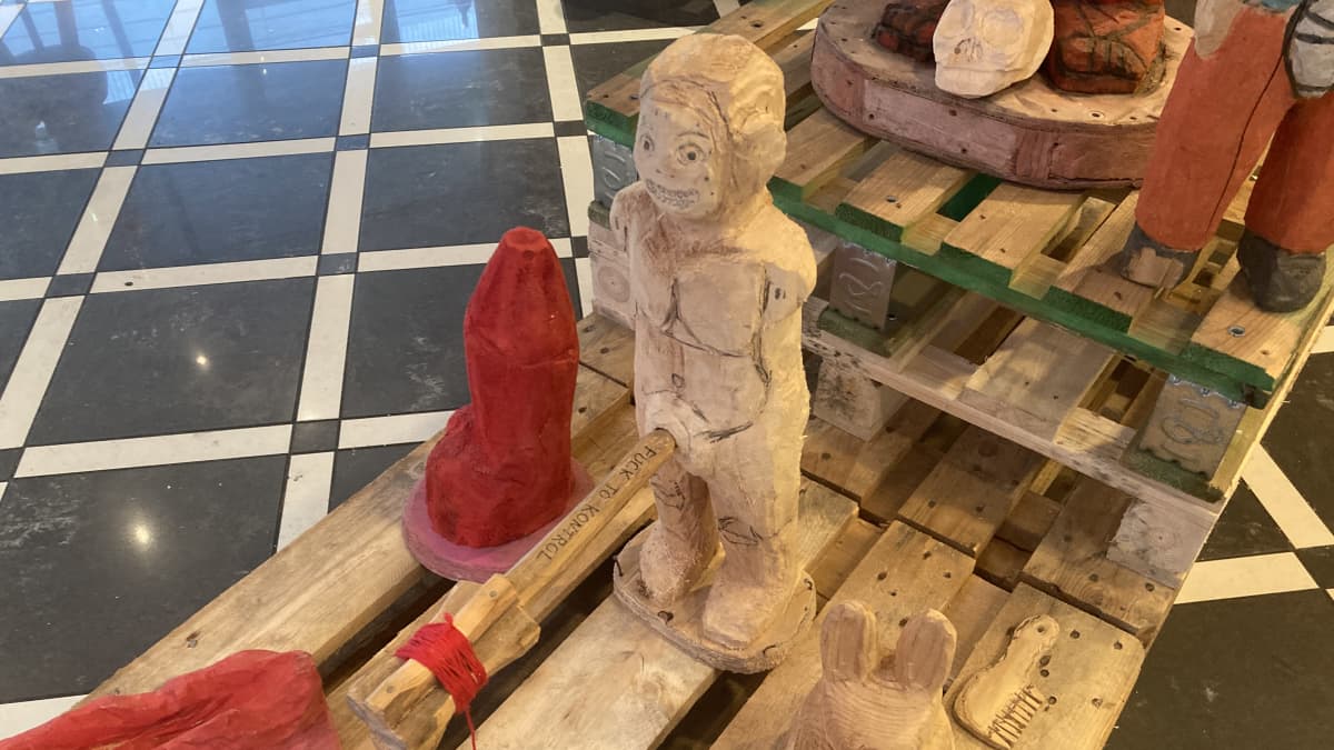 Puusta veistetty punainen penistä esittävä patsas sekä puinen veistetty mieshahmo