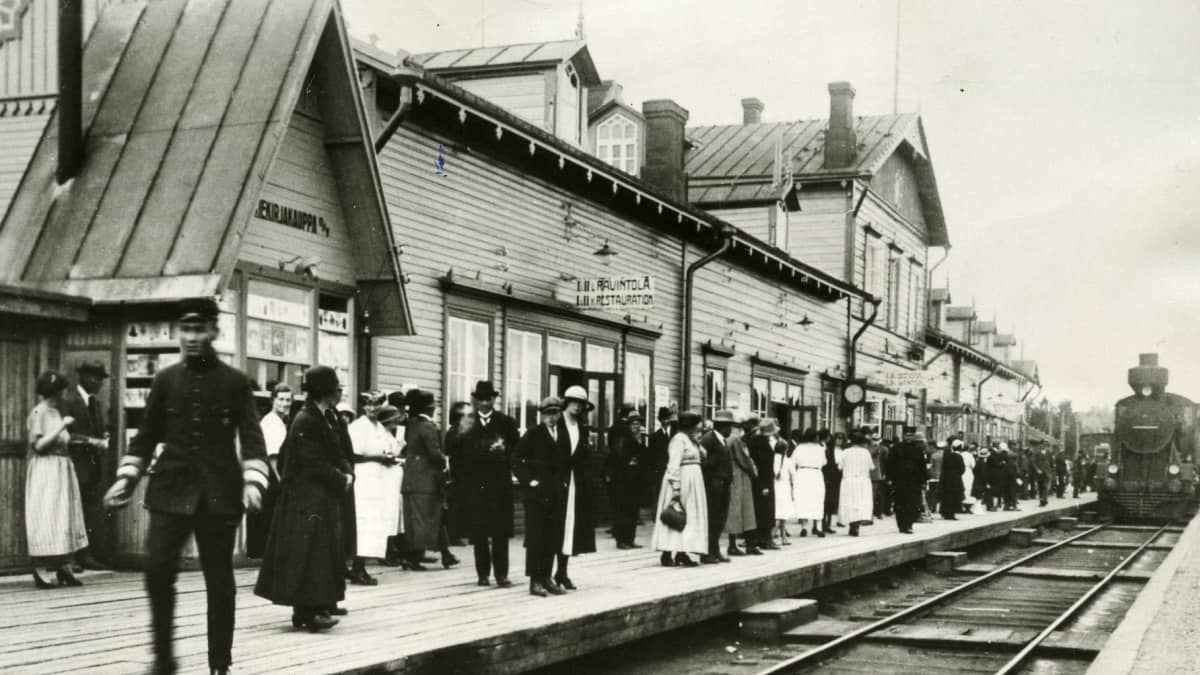 Riihimäen rautatieasema 1920-luvulla. Höyryveturi saapuu. Paljon ihmisiä asemalaiturilla. 