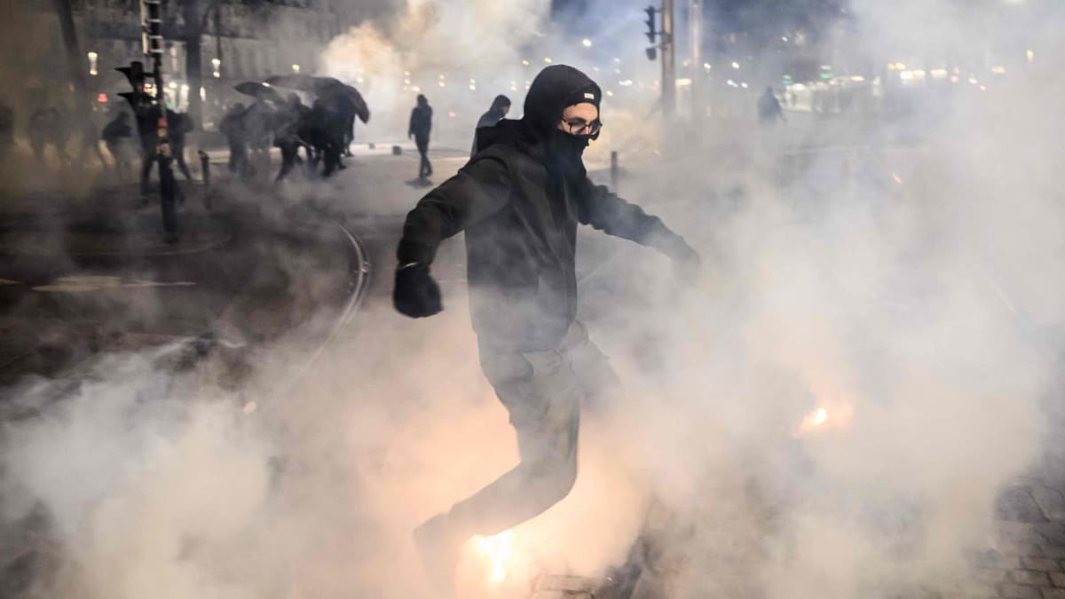Mustaan pukeutunut ja naamioitunut mielenosoittaja kulkee kyynelkaasupilven läpi öisessä Pariisissa.