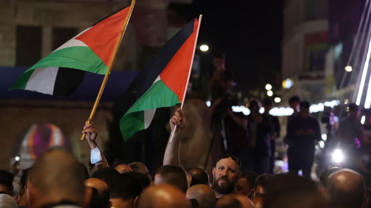 Ihmiset heiluttavat palestiinalaisten lippuja öisellä kadulla