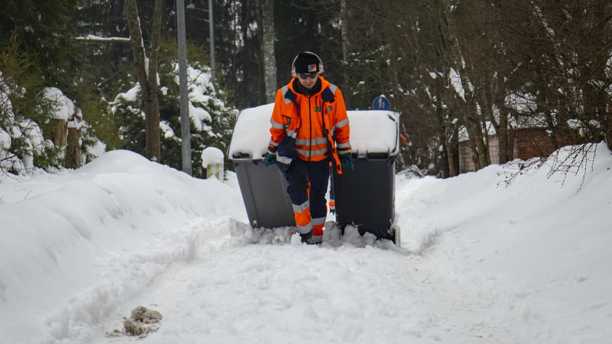 Jäteauton kuljettaja vetää roska-astioita lumimössössä.