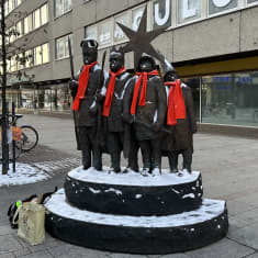 Pronssinen tiernapoikapatsas Oulun keskustassa. Tiernapohilla on oranssit kaulahuivit kaulassa. 