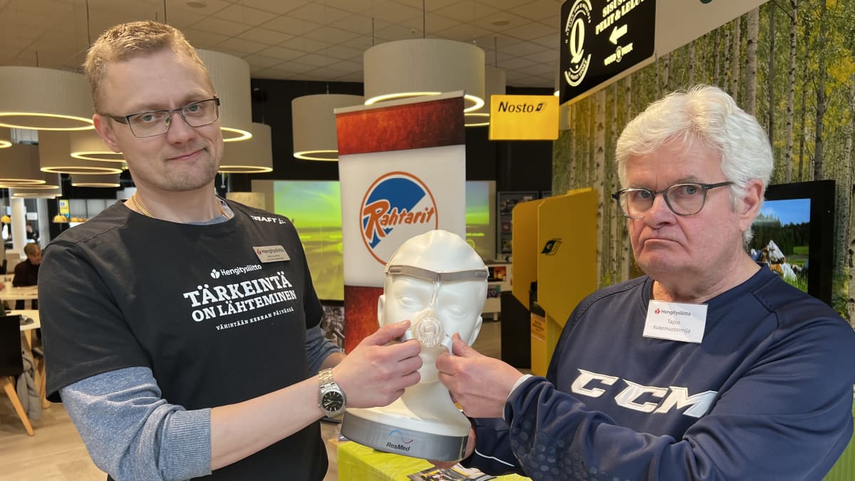 Kaksi miestä pitelee käsissään mallinuken päätä, jonka kasvoille on asetettu CPAP-maski.