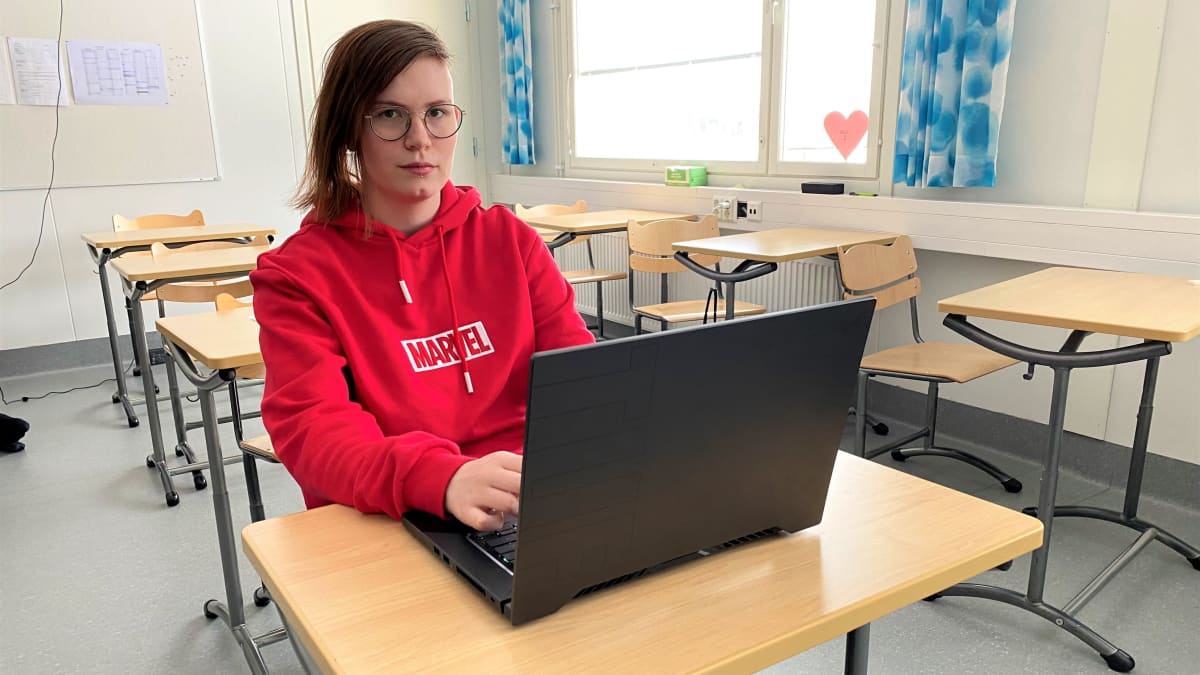 Sysmän lukion opiskelija Lumi Renvall punaisessa hupparissa pulpetin ääressä tietokone edessään.