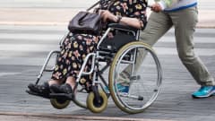Nainen työntää vanhusta pyörätuolissa.