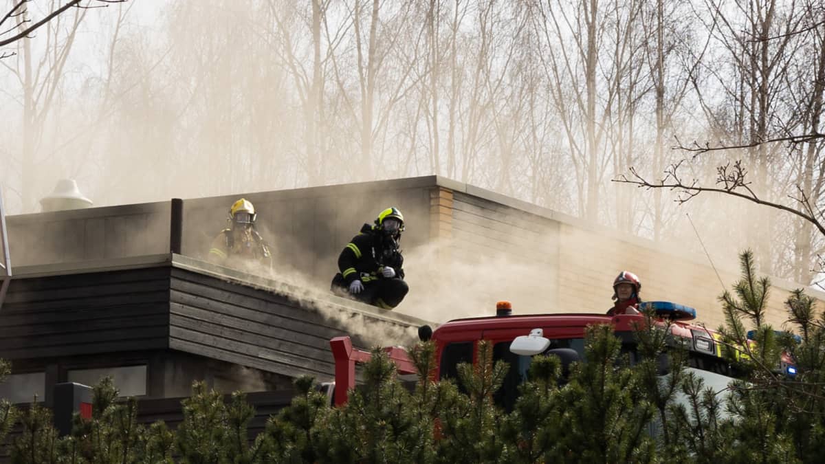 Palomiehiä seisomassa Kaukajärven seurakuntatalon katolla. Rakennuksen sisältä nousee savua.