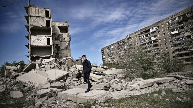 Henkilö kävelee tuhoutuneen rakennuksen edessä.