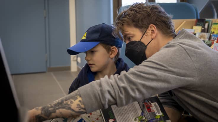 Isä ja poika kirjastossa, kirjoja kädessä.