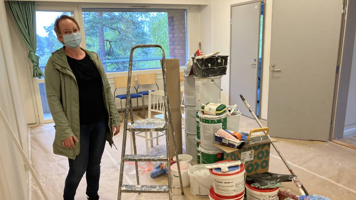 Ksaon Marika Hänninen seisoo remontoitavan huoneen keskellä. Lattialla kasa maalausvälineitä.