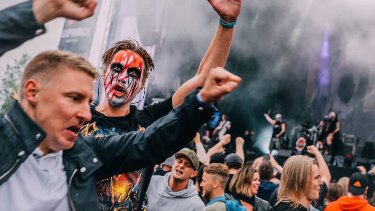 A heavy metal fan in face paint, hands up and looking at the camera during a gig during the 2022 Kuopio Rock Festival. 