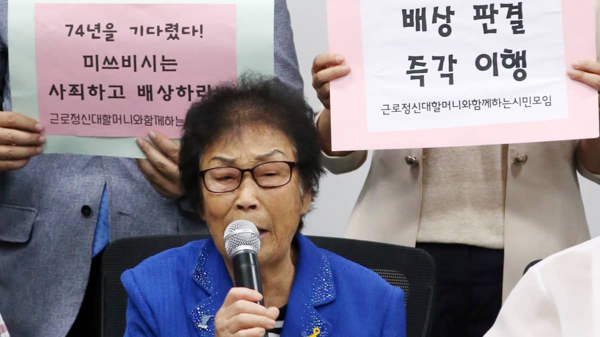 Yang Geum-deok mikrofoni kädessä, taustalla kaksi ihmistä.